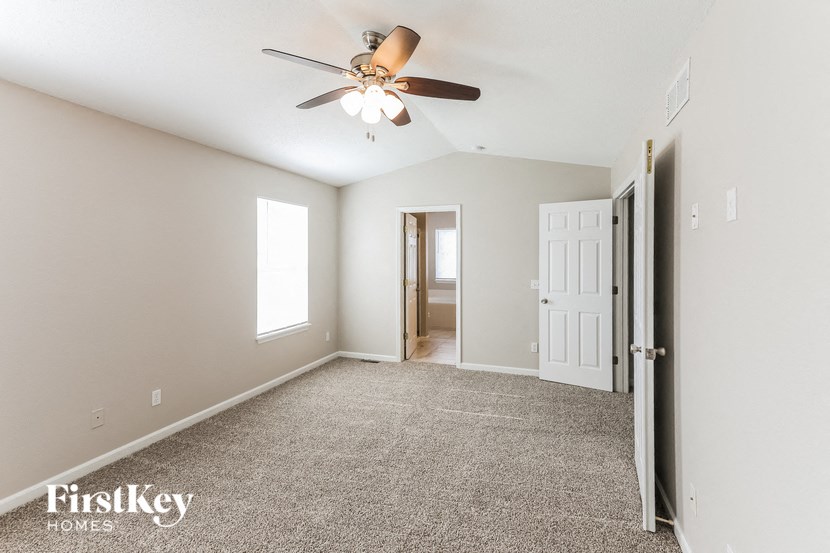 a empty living room with a ceiling fan and a door to a bathroom