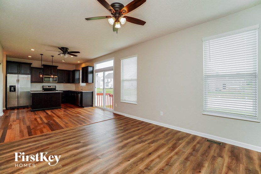 an empty living room with a ceiling fan and a kitchen