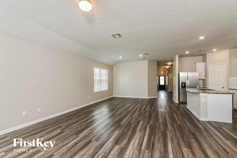 A spacious room with wooden floors and a kitchen area in the background.