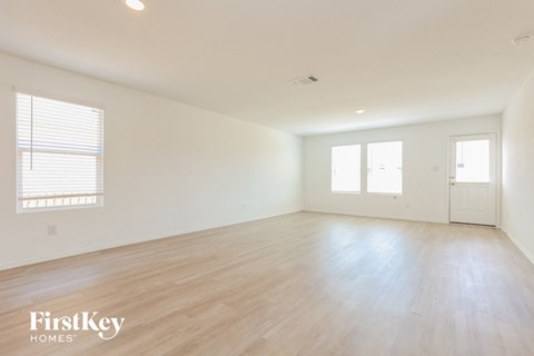 A spacious empty room with wooden flooring and white walls.