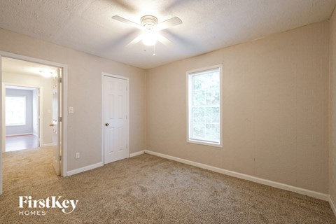 A room with a carpet floor, a ceiling fan, and a window with a view of trees.