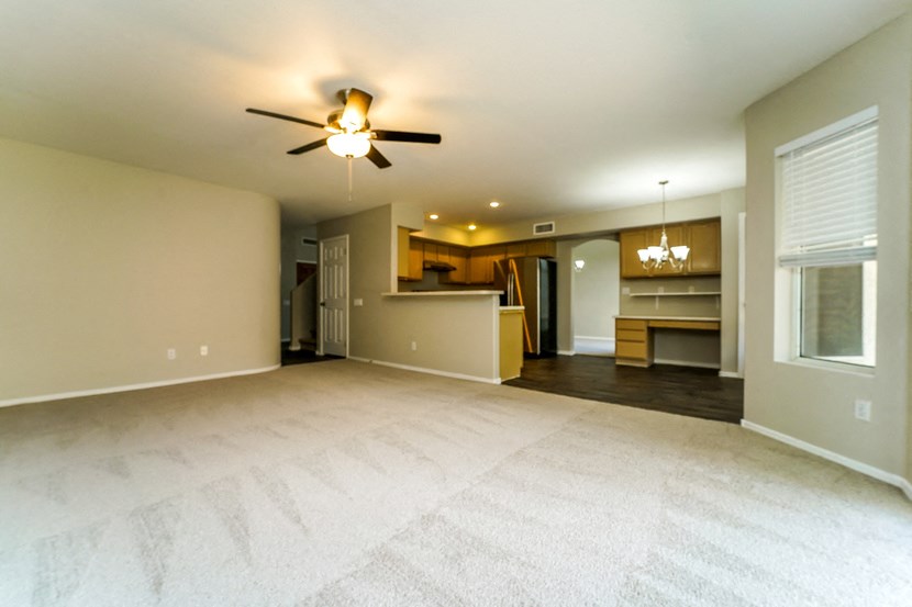 an empty living room with a ceiling fan and a kitchen
