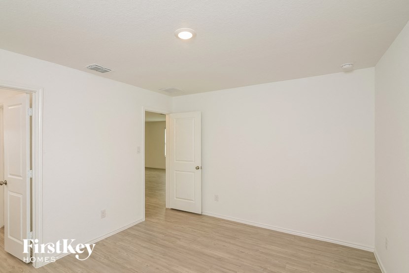 a bedroom with white walls and wood flooring and a door to a hallway