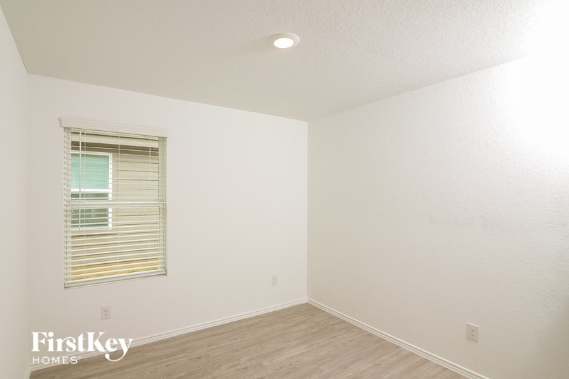 a bedroom with white walls and wood floors and a window