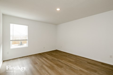 a bedroom with white walls and wooden floors and a window