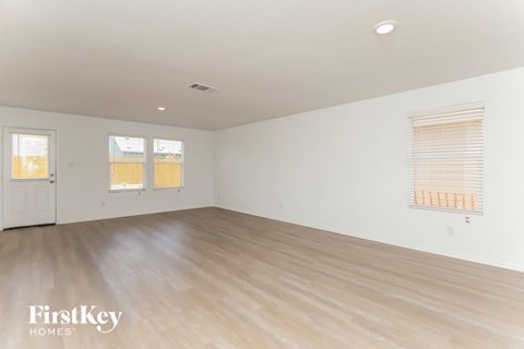 A spacious room with wooden flooring and two windows with blinds.