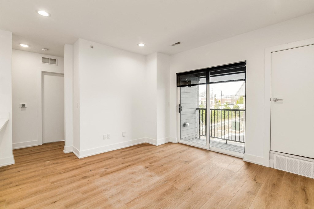 a living room with white walls and a sliding glass door to a balcony