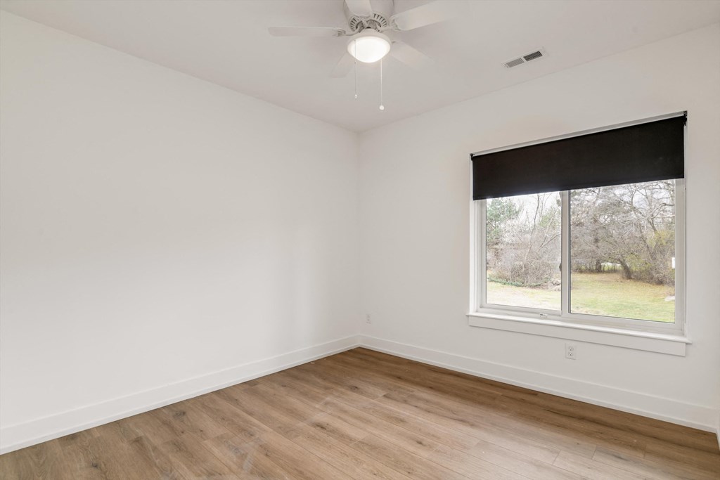 a bedroom with white walls and a window and wood floors