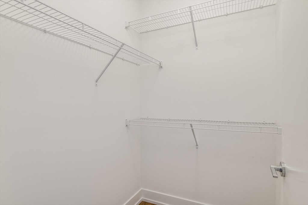 a walk in closet with white walls and a wire shelf on the wall