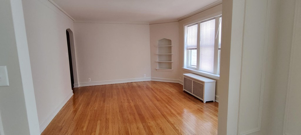 a living room with a wooden floor and a window and a radiator and a shelf