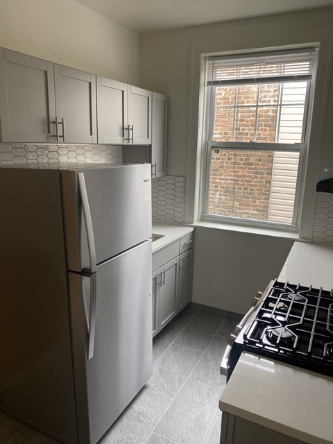 A kitchen with a stainless steel refrigerator and a window with blinds.