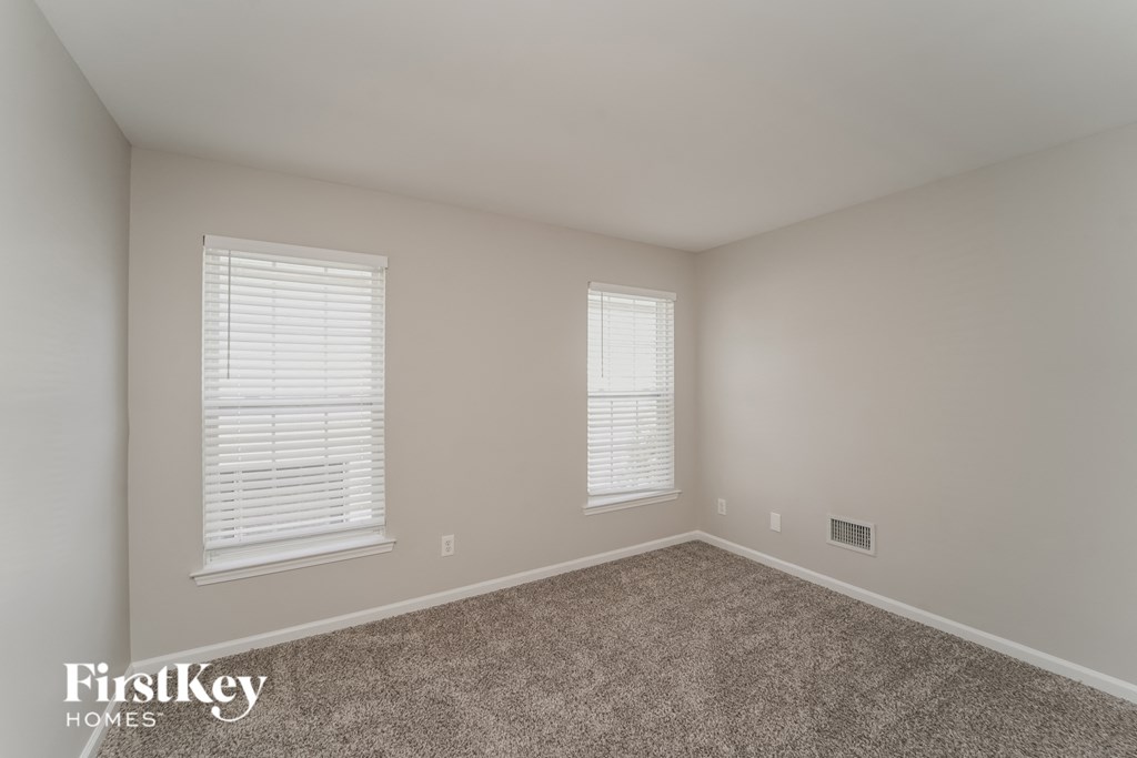 A room with a carpeted floor and two windows with blinds.