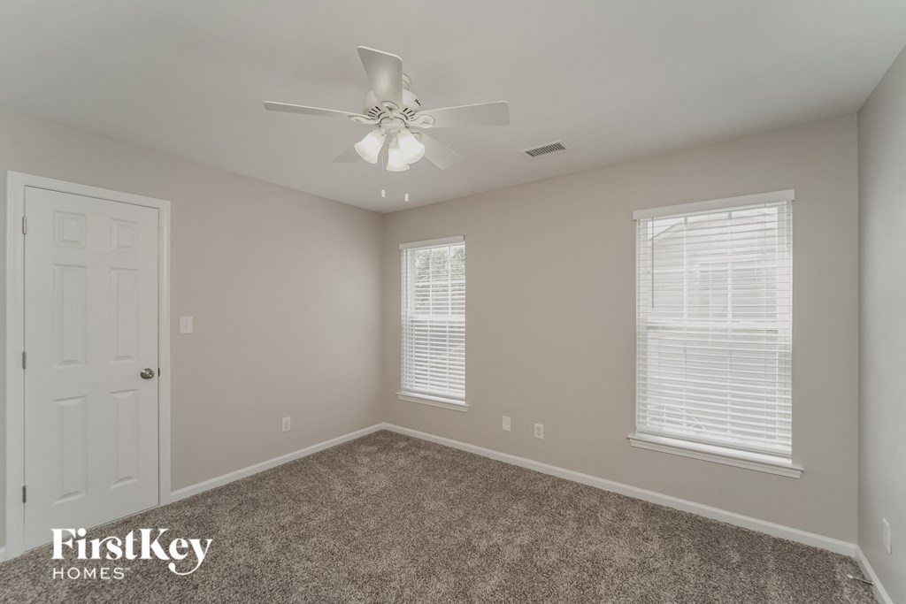 A room with a ceiling fan and two windows.
