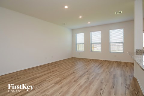 A spacious room with wooden flooring and three windows.