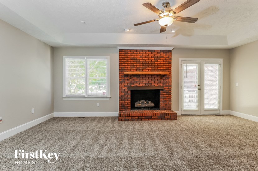 an empty living room with a brick fireplace and a ceiling fan
