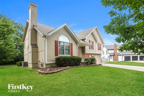 a beige house with red shutters and a green lawn