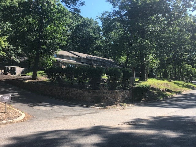 A tree-lined street with a stone wall and a house in the background.