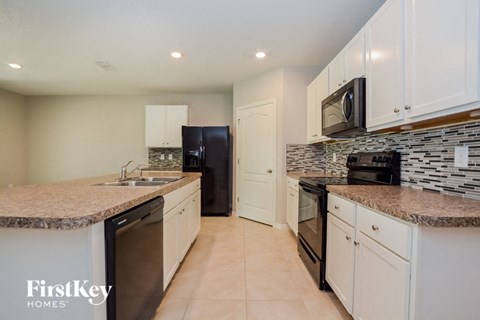 A kitchen with a black refrigerator and white cabinets.