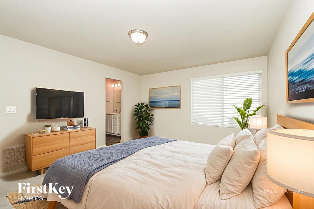 A bedroom with a bed, a dresser, a television, a plant, and a painting on the wall.