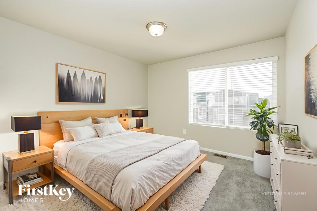 A bedroom with a large bed, a nightstand with a lamp, and a window with blinds.