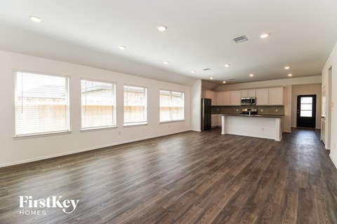 A spacious room with wooden floors and a kitchen area in the background.