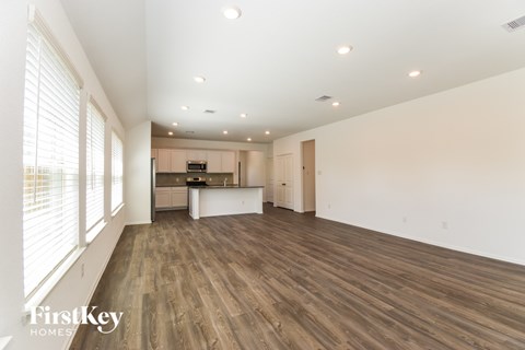 A spacious room with wooden flooring and a kitchen area in the background.