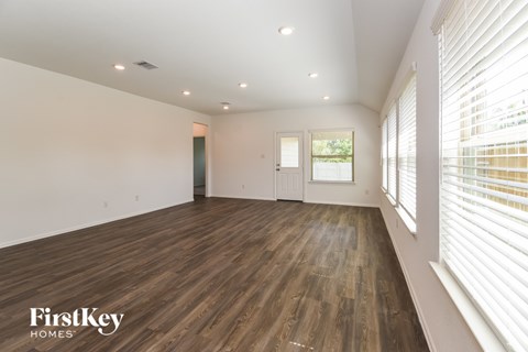 A spacious room with wooden flooring and a large window with blinds.