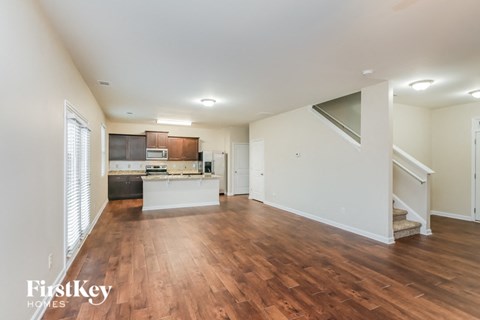 A spacious living room with wooden floors and a staircase leading to another room.