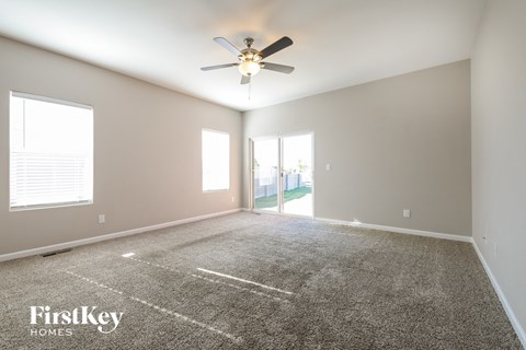 the spacious living room with carpeted flooring and a ceiling fan