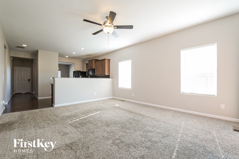 an empty living room with a ceiling fan and a kitchen