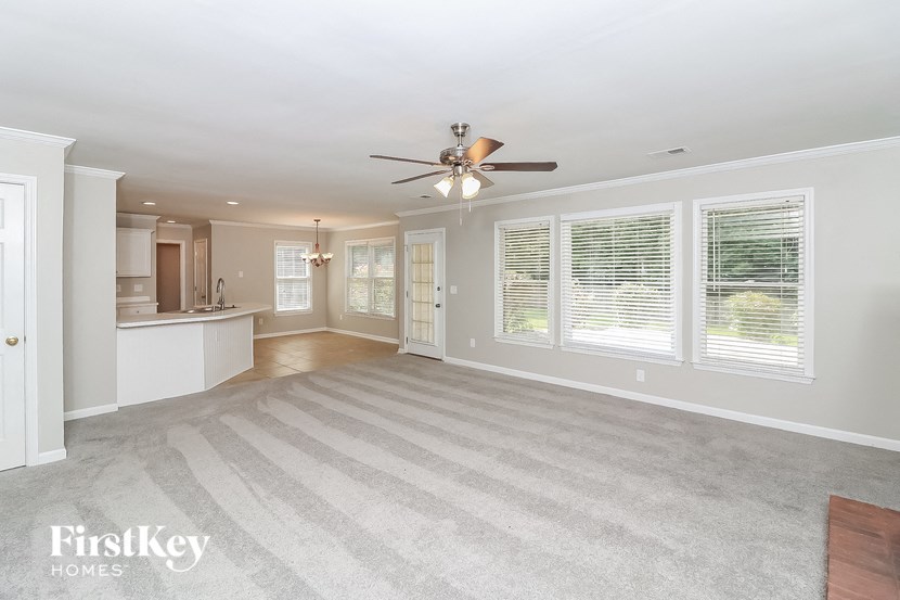 an empty living room with a ceiling fan and a kitchen