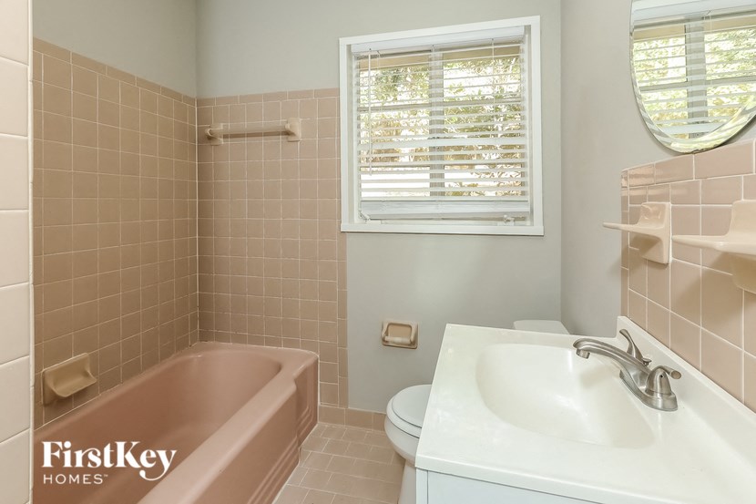 A bathroom with a pink bathtub, white toilet, and sink.