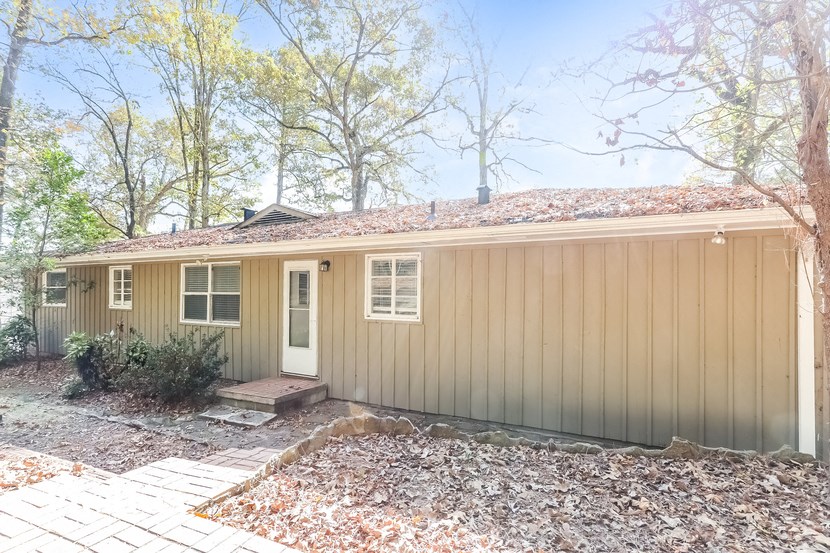 A house with a brown siding and a white door is surrounded by trees.