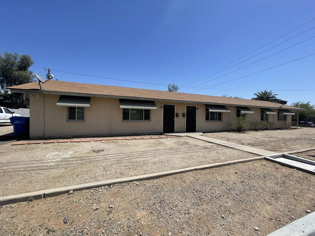 a tan house with a dirt lot and a parking lot