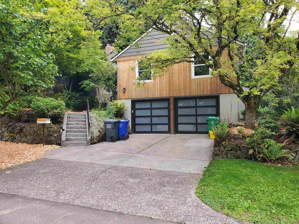 A modern house with a wooden exterior and a grey roof is surrounded by greenery.