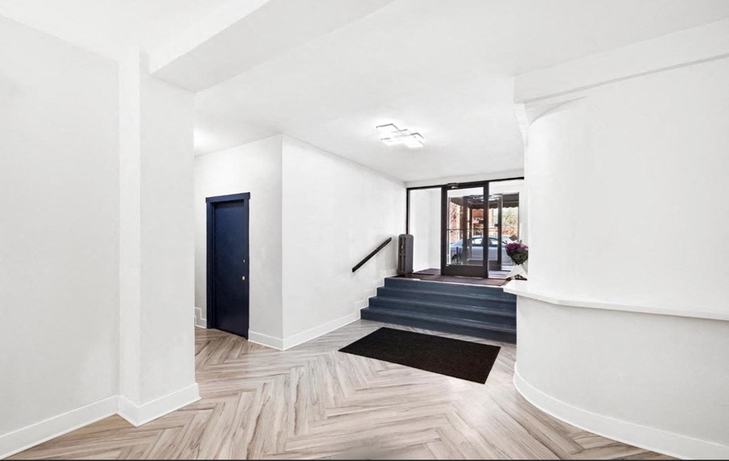 A hallway with a black mat on the floor leading to a staircase.