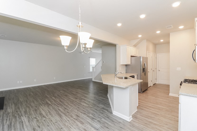 an open kitchen and living room with a kitchen island and a stainless steel refrigerator