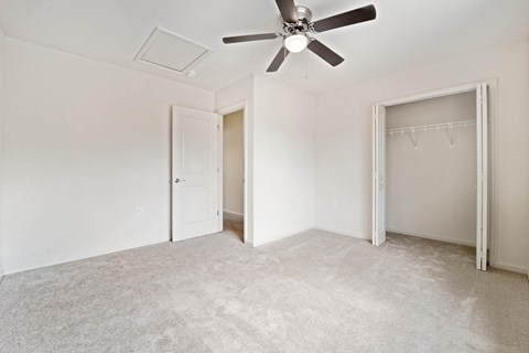 an empty bedroom with a ceiling fan and closet