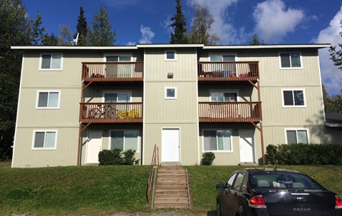 A black car is parked in front of a tan apartment building.