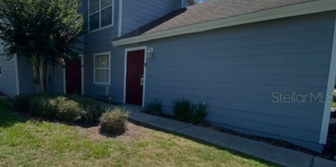 A grey house with a red door and a tree in front.
