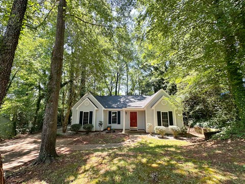 A small white house with a red door is surrounded by trees.