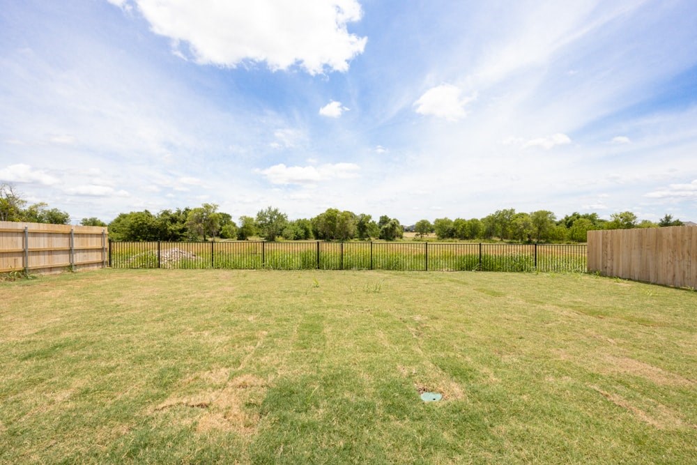 the backyard is fenced in with a fence and green grass