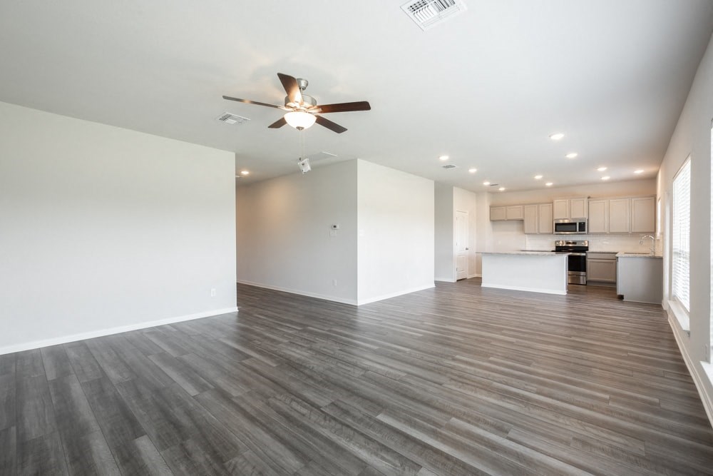 an empty living room with a ceiling fan and a kitchen
