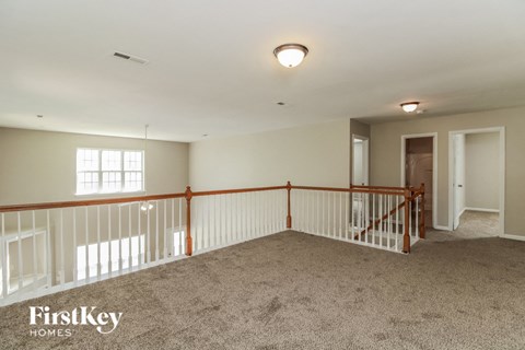 A spacious room with a carpeted floor and a balcony with white railings.