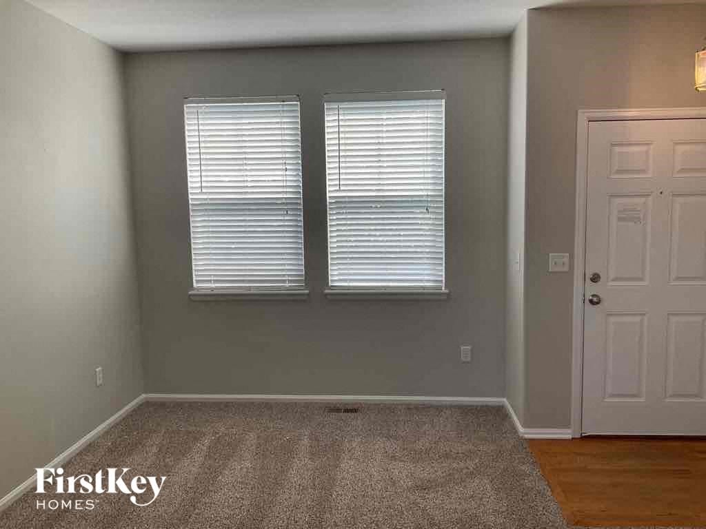 A room with a carpeted floor, two windows with blinds, and a white door.