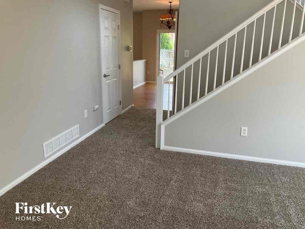 A hallway with a carpeted floor and a staircase with white railings.