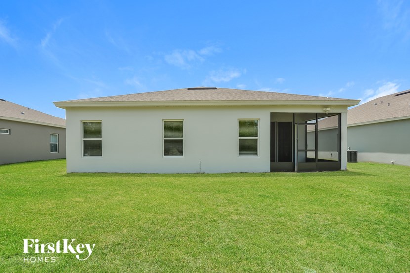A white house with a black door and windows is surrounded by a grassy lawn.