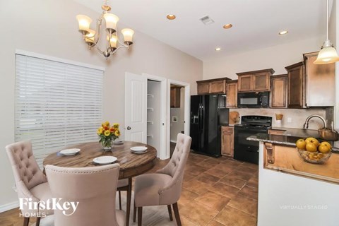 A dining room with a wooden table set for two and a kitchen area with a refrigerator, microwave, and oven.