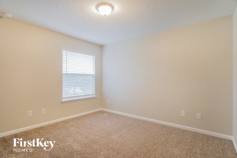 the spacious bedroom with carpeted flooring and a window