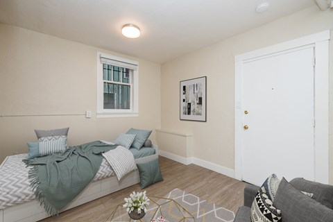 A bedroom with a bed, pillows, a blanket, a couch, a coffee table, and a painting on the wall.